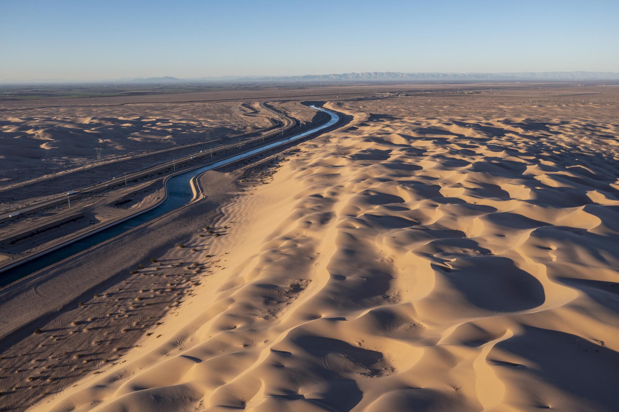 A water canal cuts through sand dunes. 