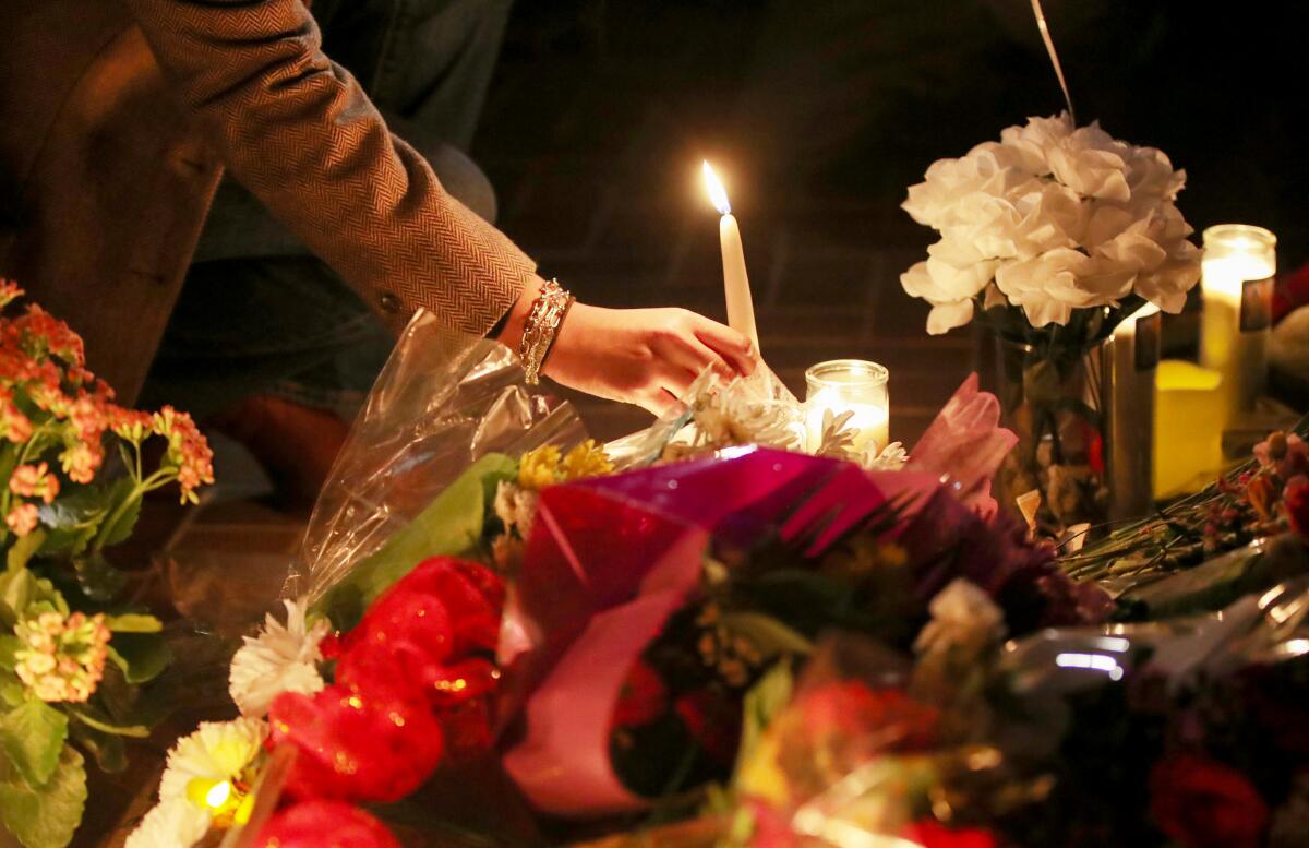 A person holds a lit candle next to bouquets of flowers 