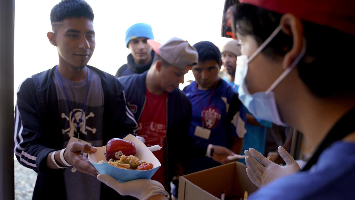 A volunteer with World Central Kitchen at El Barretal migrant shelter in Tijuana helps pass out the hot meals consisting of a three cheese enchilada and fruit.