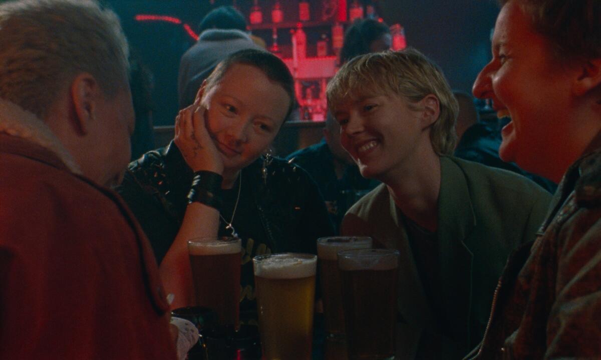 Two smiling women at a pub table with friends, with pints of beer in front of them