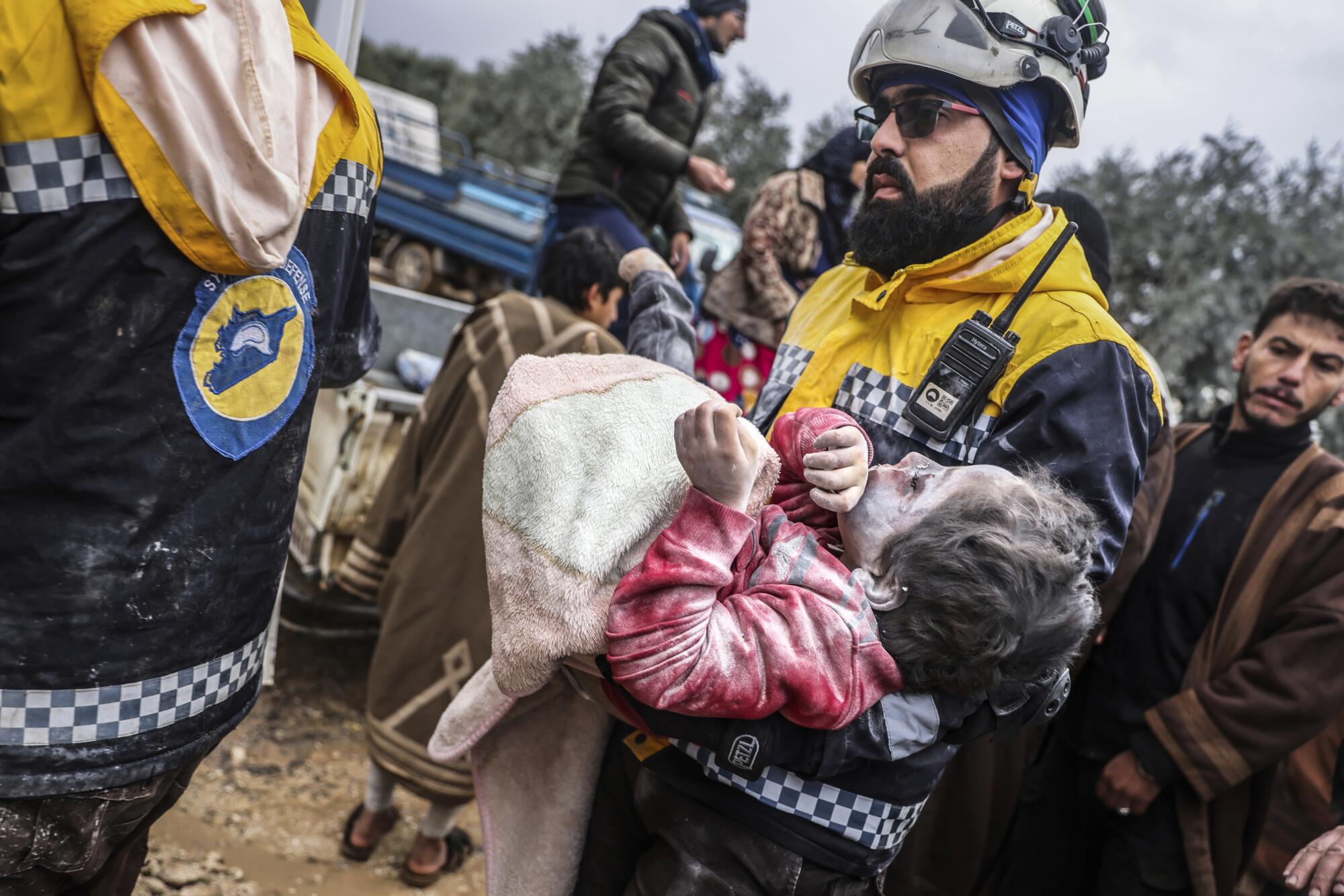 A man in rescue gear carries a dust-covered young girl in his arms