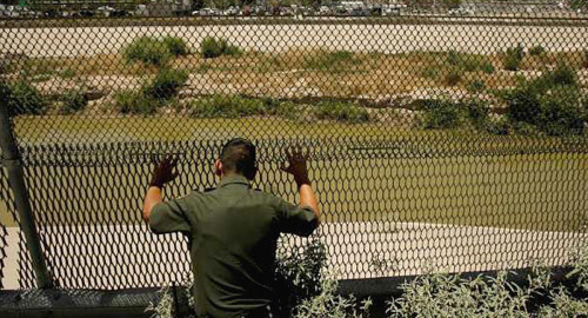 A U.S. Border Patrol agent scans the Rio Grande through a fence after seeing four people attempt to cross the US-Mexico border illegally.