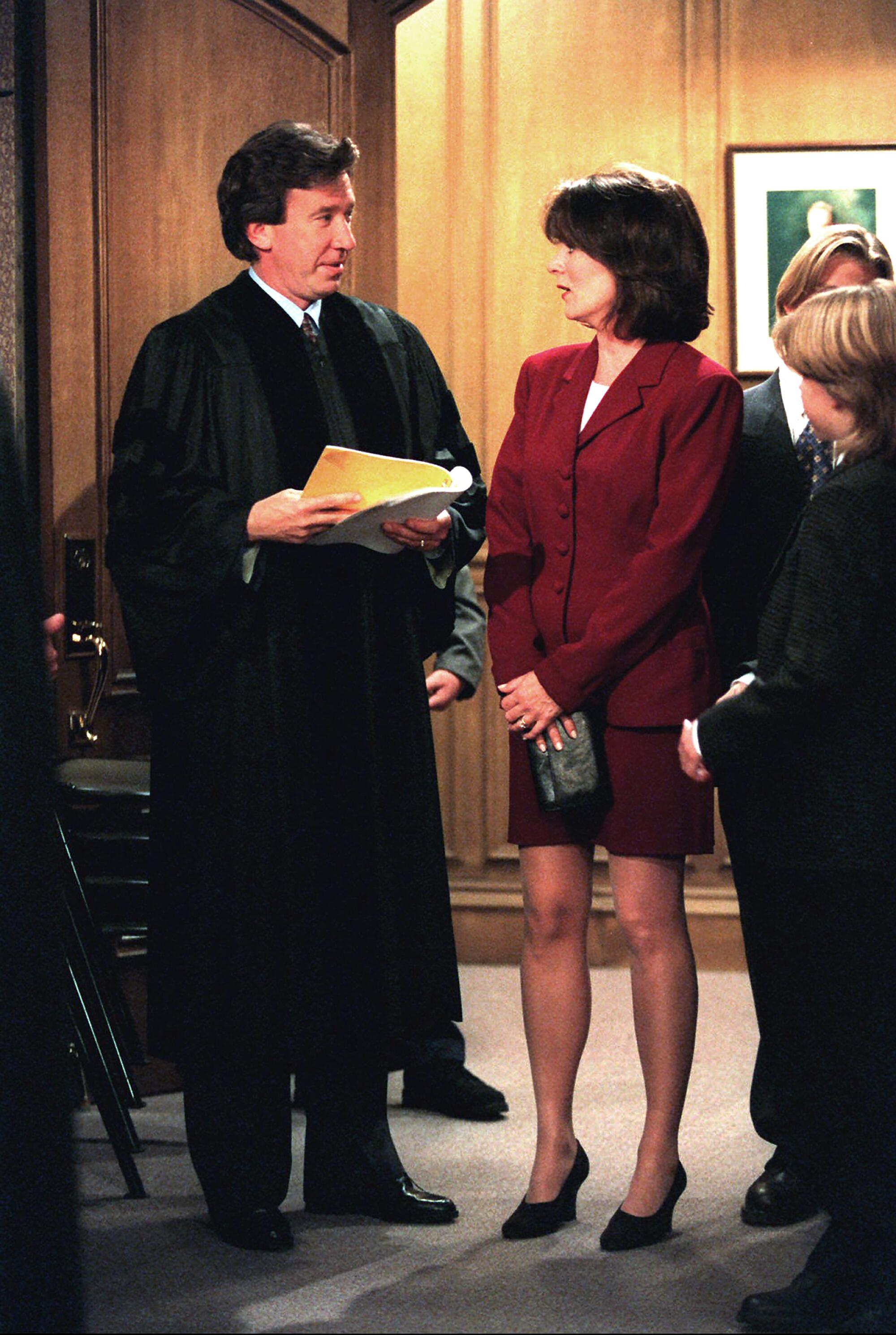 A man in a black robe stands next to a woman in red suit.