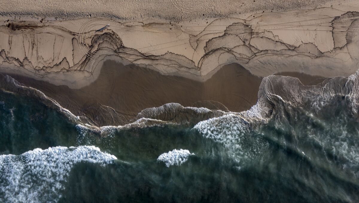 An aerial view of the October 2021 oil spill washing ashore in Huntington Beach with birds feeding at the water's edge.