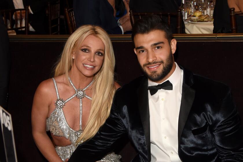 Britney Spears and Sam Ashgari in formalwear smile while sitting at a table