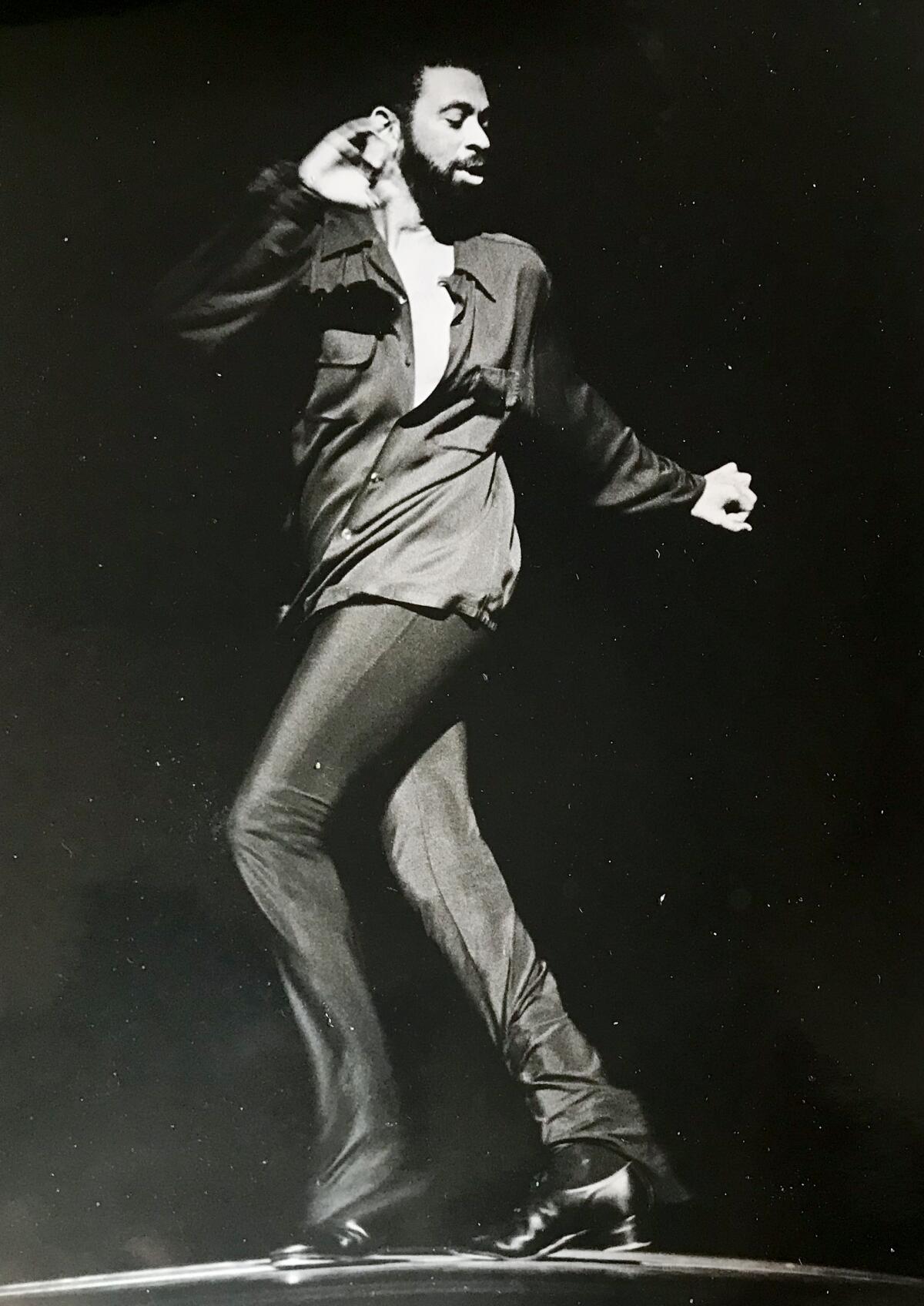 Maurice Hines strikes a dance pose, standing and twisting to his left, in tight-fitting dark shirt and slacks.