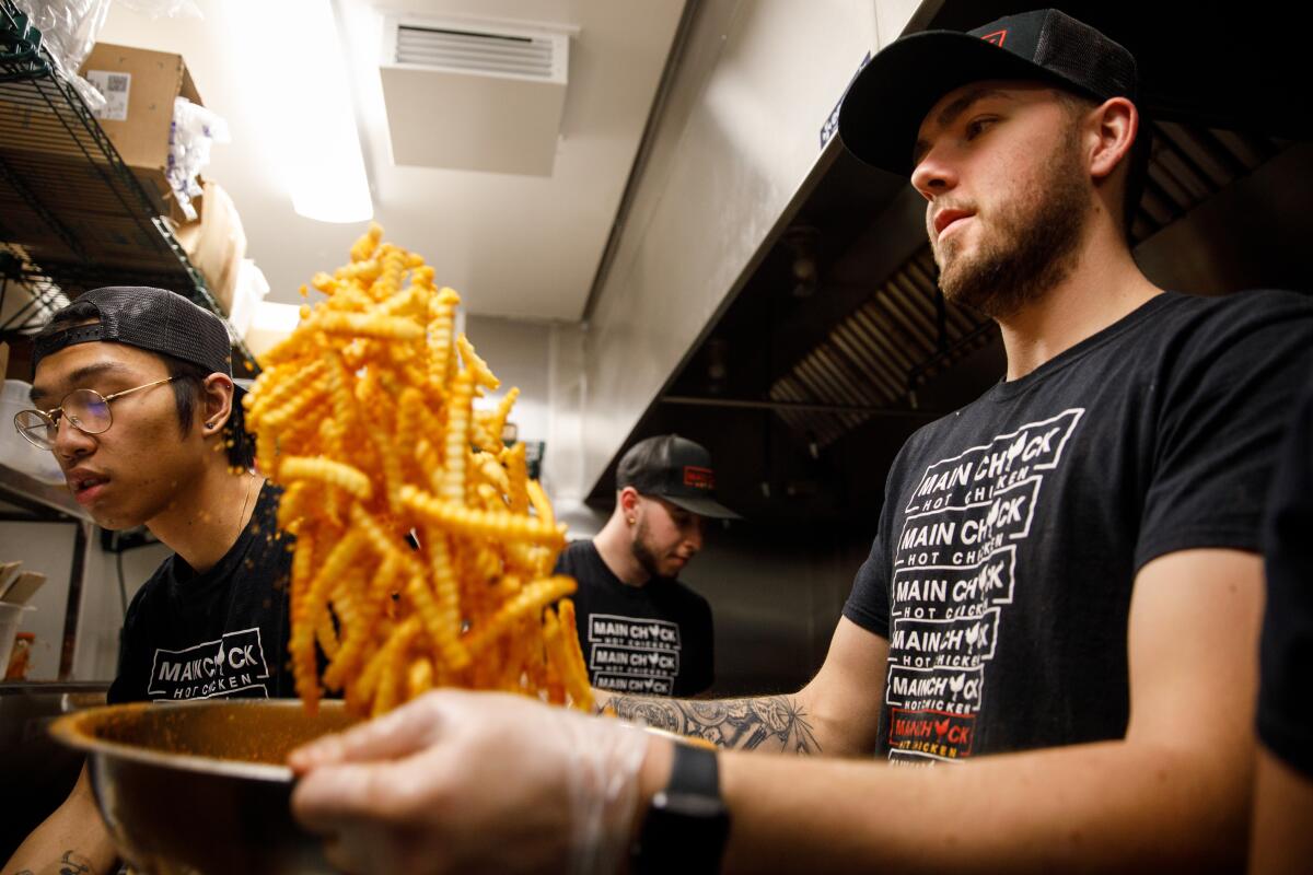 Kevin Popok, right, tosses fries with seasonings as Ethan Valenzuela, left, prepares Nashville-style hot fried chicken sandwiches and fries in the Main Chick Hot Chicken kitchen at Colony