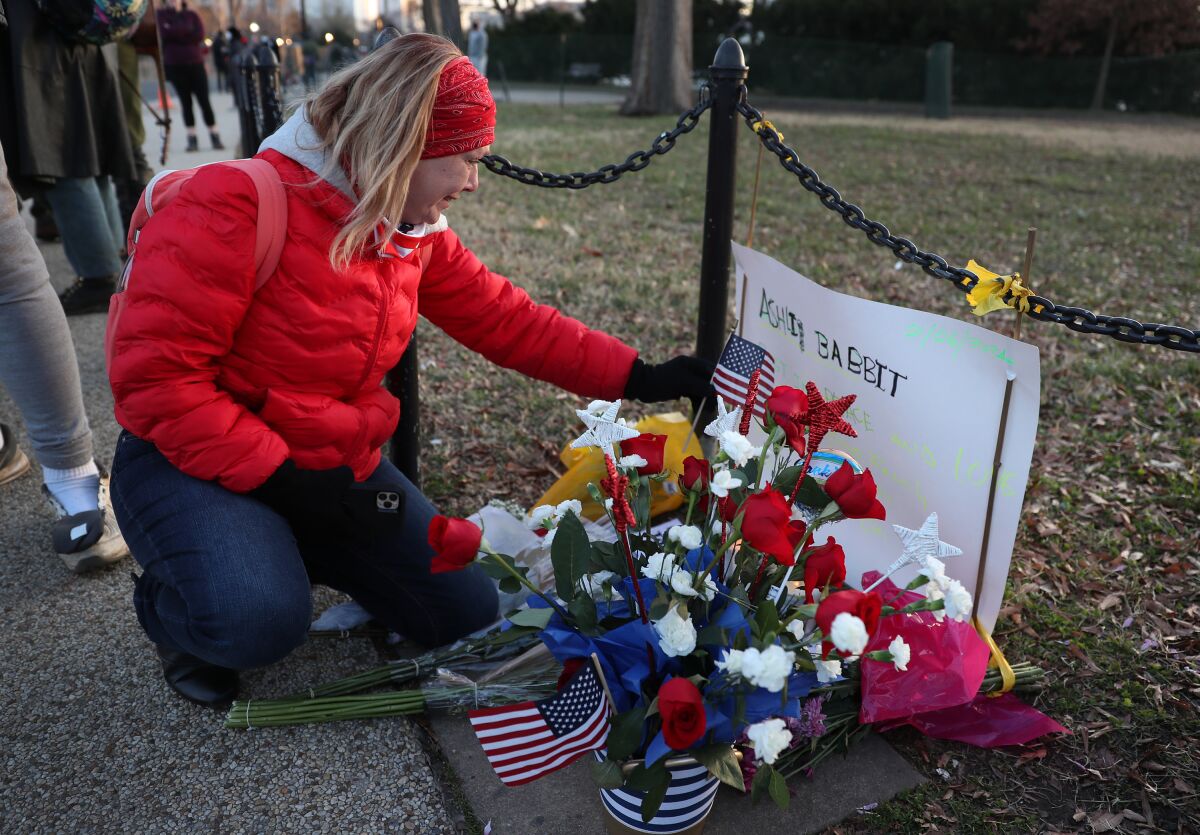 A woman in a red winter jacket kneels down to put a small U.S. flag on a memorial with flowers and a handmade sign