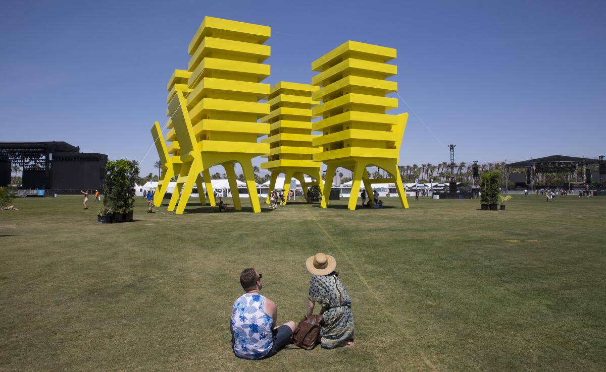 Several chair-like structures bearing towering buildings, all painted bright yellow, stand on a grassy lawn