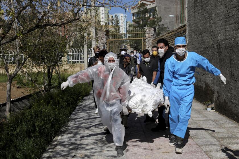 FILE — In this March 30, 2020 file photo, people wearing protective clothing carry the body of a victim who died after being infected with the new coronavirus at a cemetery just outside Tehran, Iran. Even as both face the same invisible enemy in the coronavirus pandemic, Iran and the U.S. remain locked in retaliatory pressure campaigns that now view the outbreak as just the latest battleground. (AP Photo/Ebrahim Noroozi, File)