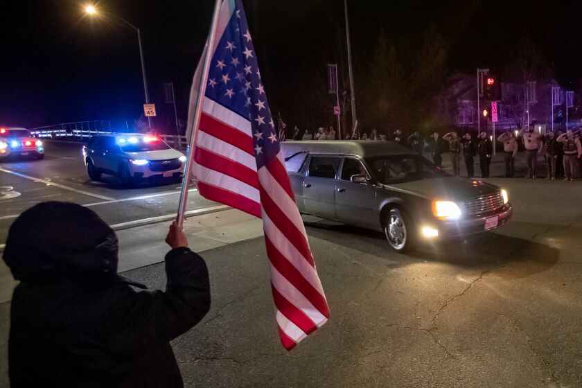 WILDOMAR, CA -JANUARY 13, 2023: Riverside County Sheriff Deputies salute and residents hold flags as a procession for fallen Riverside County Deputy Darnell Calhoun passes by as his body is taken away in hearse from Inland Valley Medical Center on January 13, 2023 in Wildomar, California. Calhoun was killed in the line of duty responding to a domestic violence call in Lake Elsinore Friday afternoon(Gina Ferazzi / Los Angeles Times)