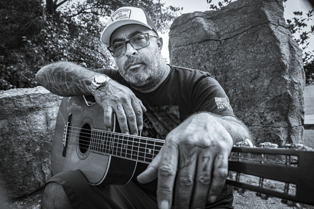 A man with tattoos holding an acoustic guitar.