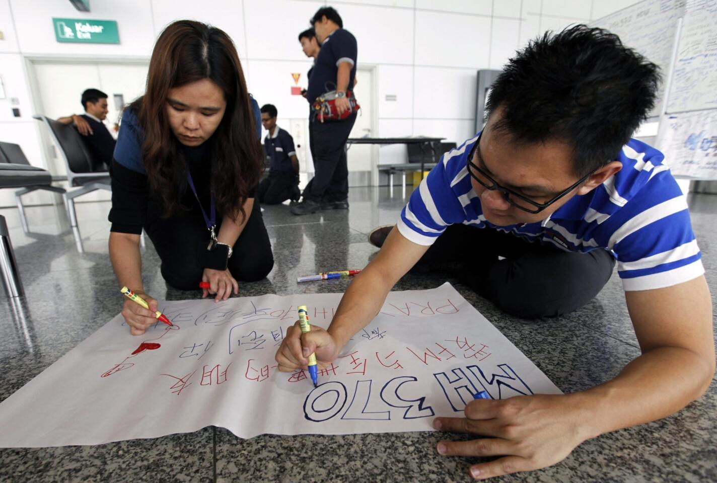 People write a message for the passengers of the missing Malaysian Airline plane, on a banner at Kuala Lumpur International Airport.