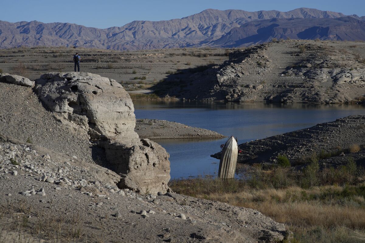 A man stands on a hill overlooking Lake Mead, a boat lodged in the mud facing upward