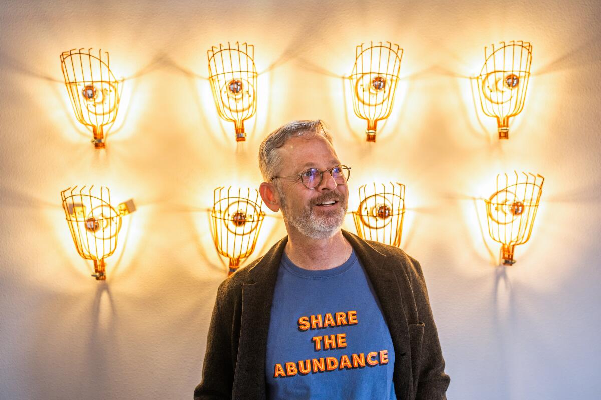 A man wearing a T-shirt with the words "Share the Abundance" stands in front of a light sculpture