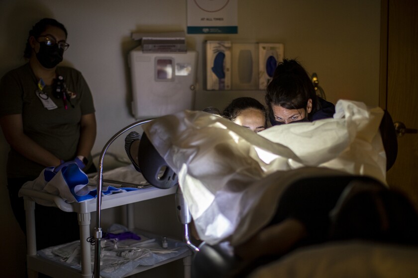 A doctor and assistant working under surgical draping on a patient whose feet are in medical stirrups