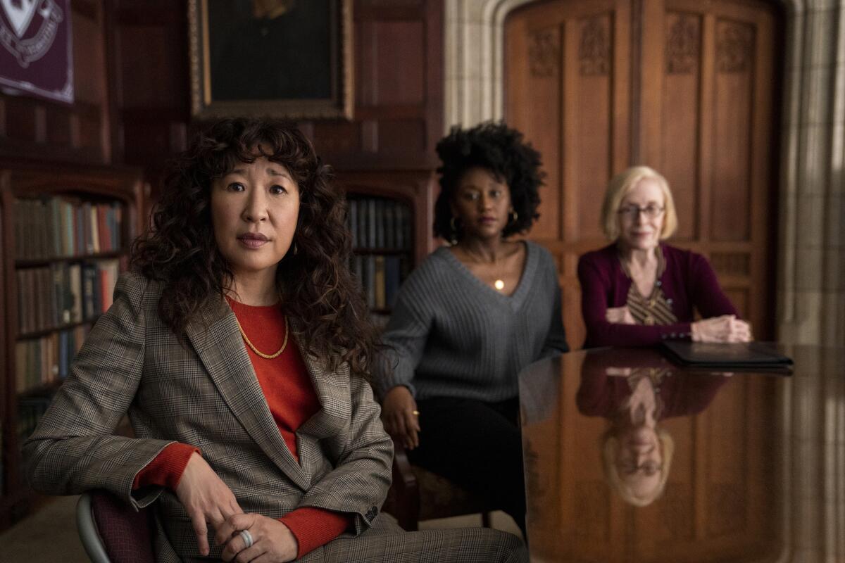 Three women sit at a conference room table in a wood-paneled room.