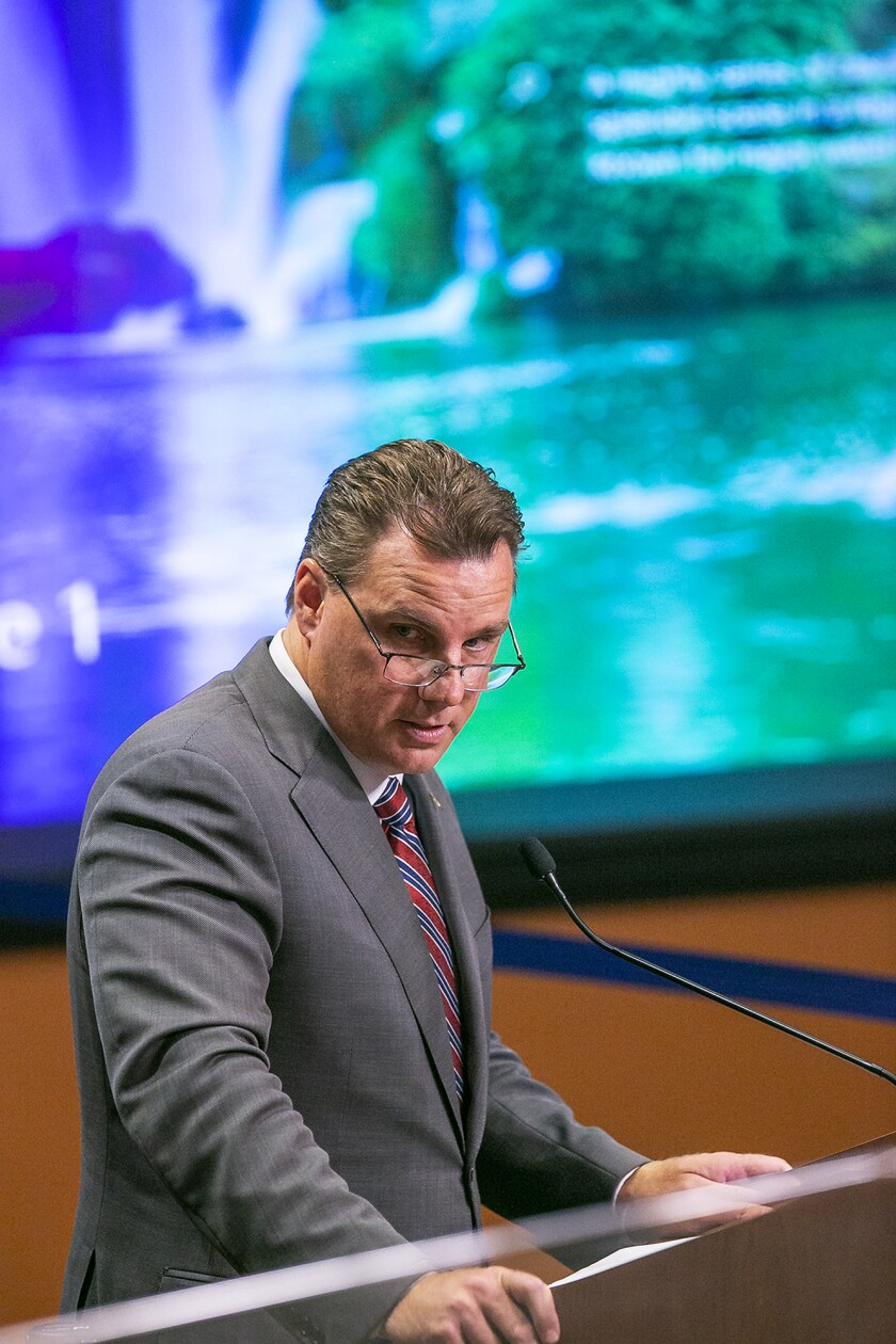 A man in a suit and tie stands before a microphone