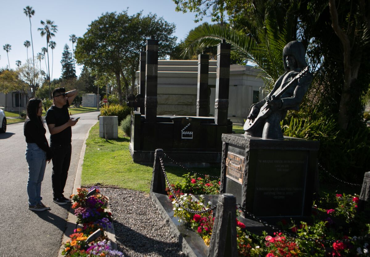 People walk by the grave of Johnny Ramone, an American guitarist and songwriter, at the Hollywood Forever Cemetery.