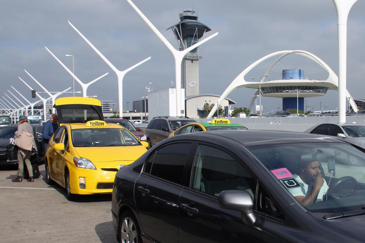 A car with Uber and Lyft stickers leaves the departures area of LAX, with taxis behind it, last month.