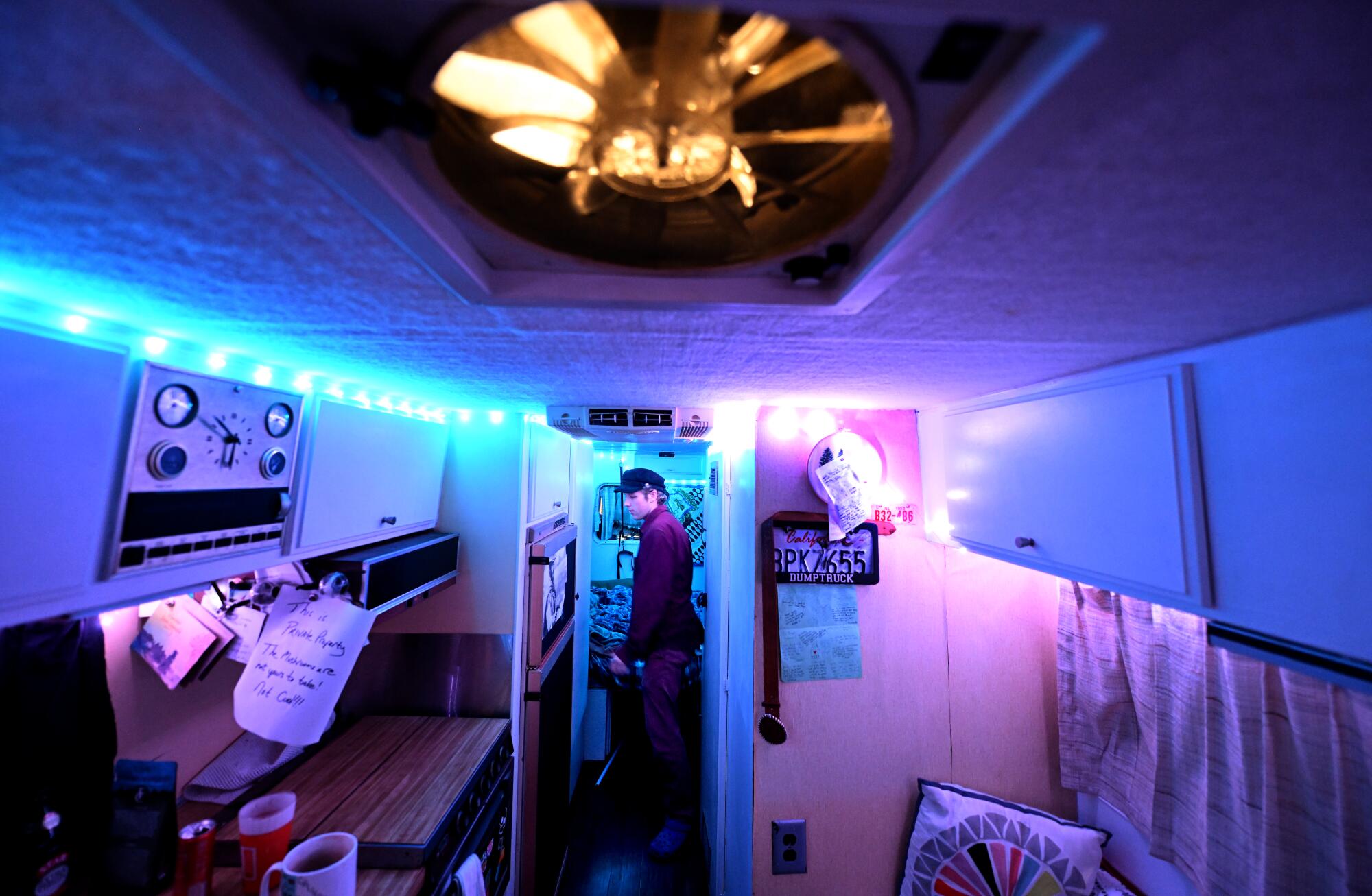 A person inside a recreational vehicle with pink and blue lighting.