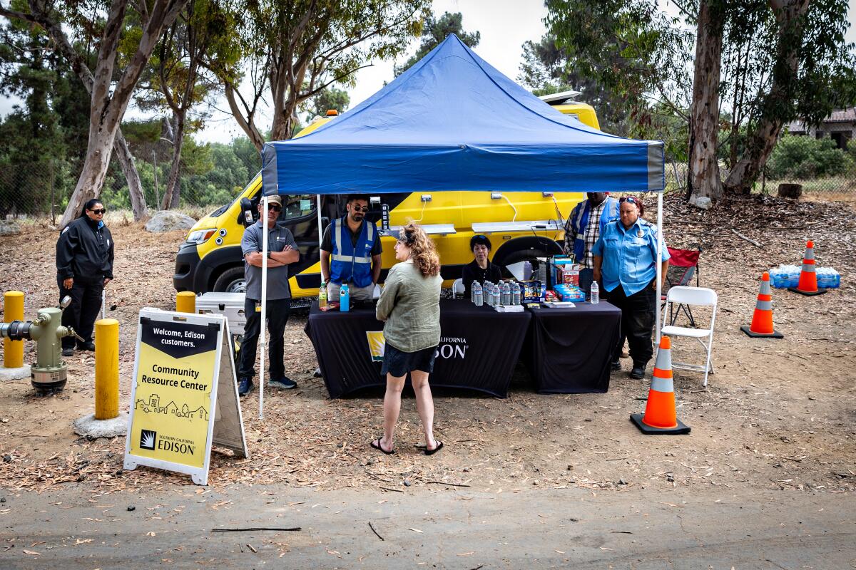 People stand under and near a portable canopy, where water bottles and other items sit on tables.