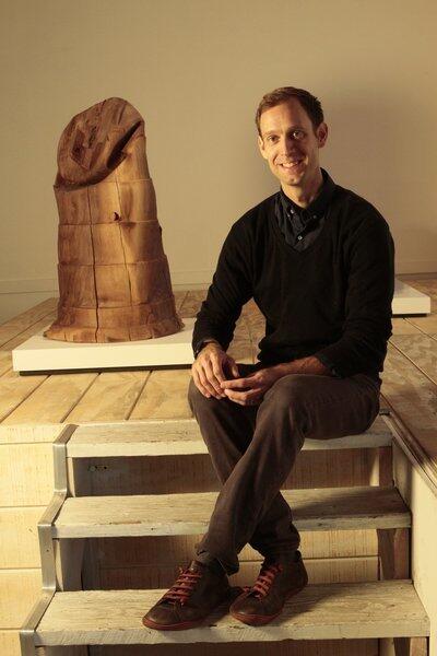 Morgan MacLean, photographed during a break in preparations for the show at Reform Gallery in L.A. Behind him: a wood sculpture of a drum traffic barrier known as a channelizer, carved over six years from a 1,000-pound walnut log. "You cannot cast these shapes out of wood," he said. "The beauty of them is knowing that they have been made out of a solid piece of material."