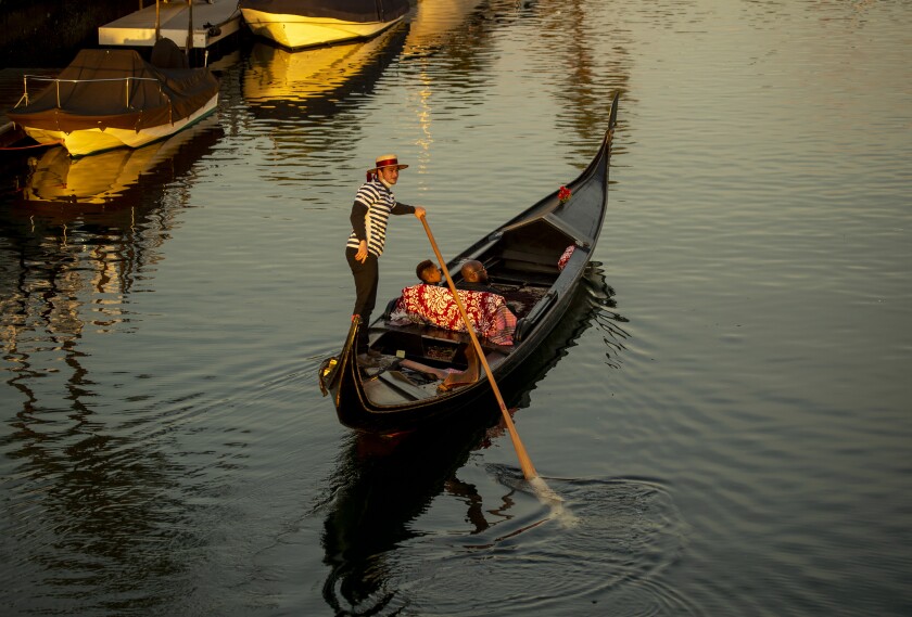 Try This Valentine's Day Road Trip In The California Desert - Los Angeles Times 7 A couple sit on a gondola in the water. In back of them, a man in a striped shirt and wide-brimmed hat holds a long oar.