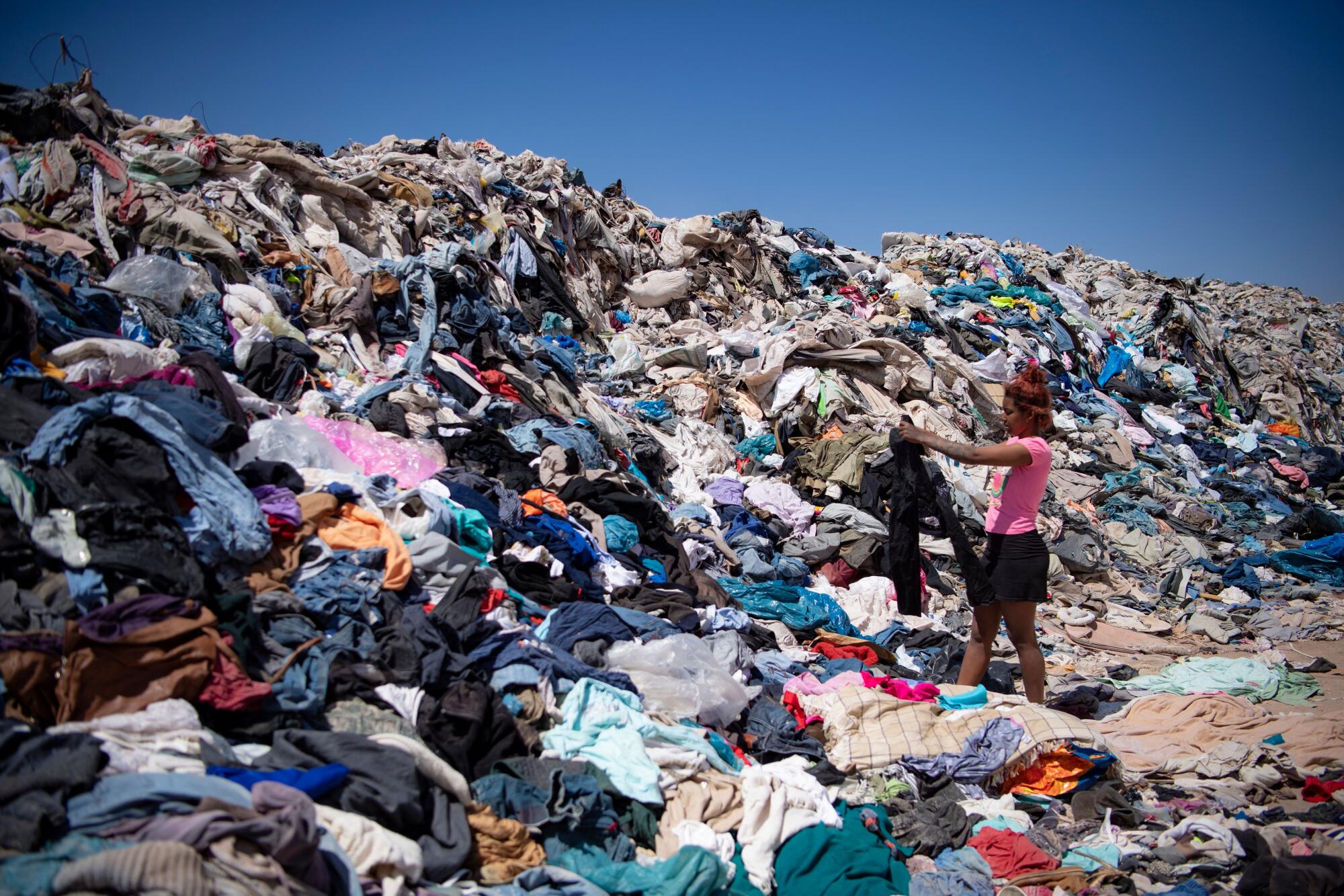 A woman stands by a towering pile of fabric.