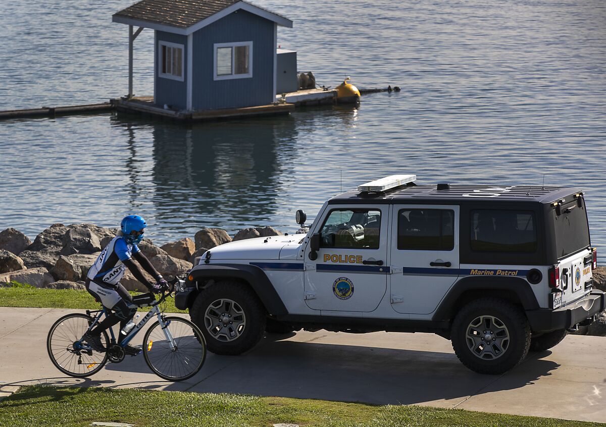 A Long Beach Beach police jeep drives past a bicyclist near the water. 