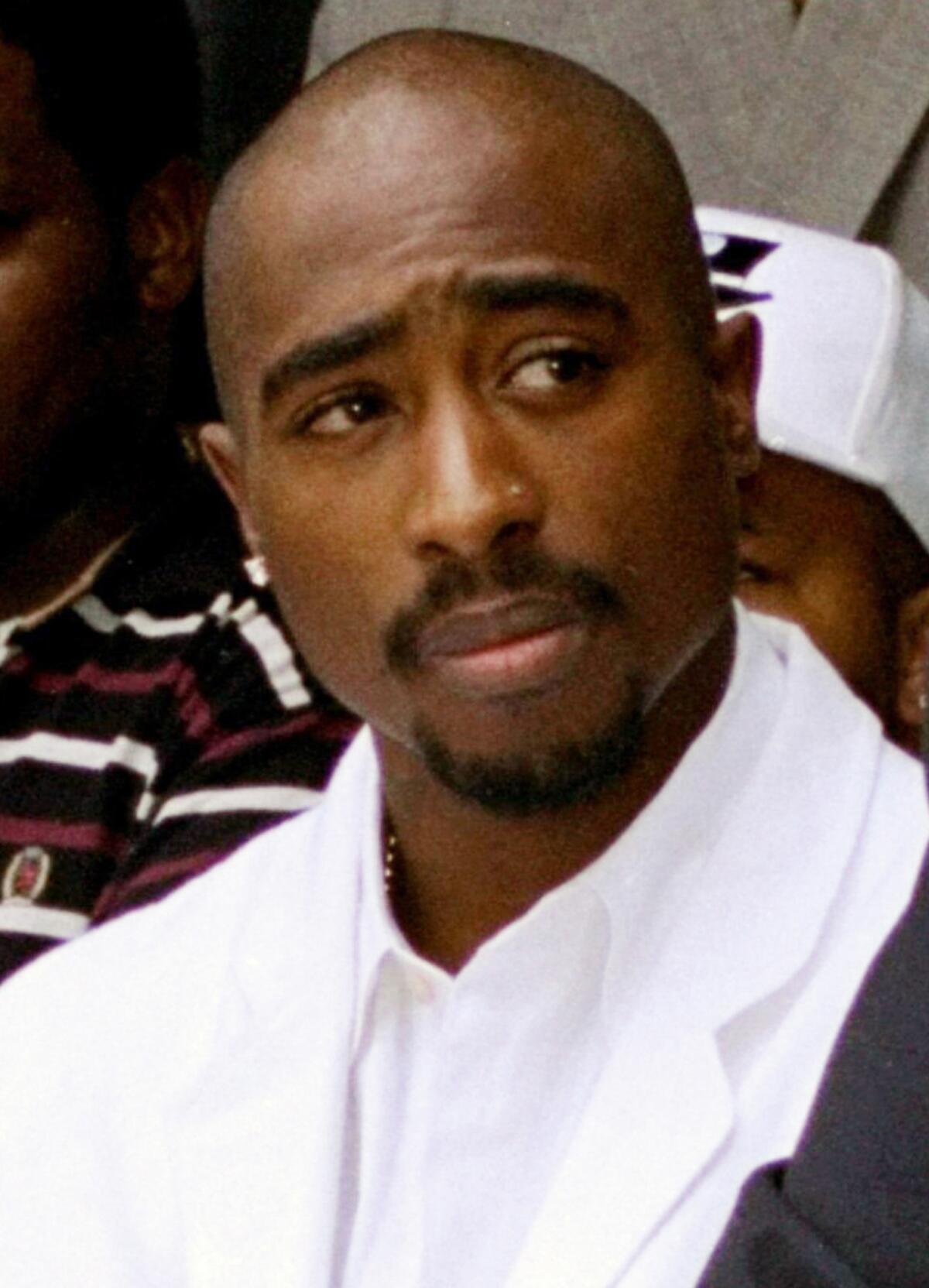 Tupac Shakur wearing a white suit and looking to his left.