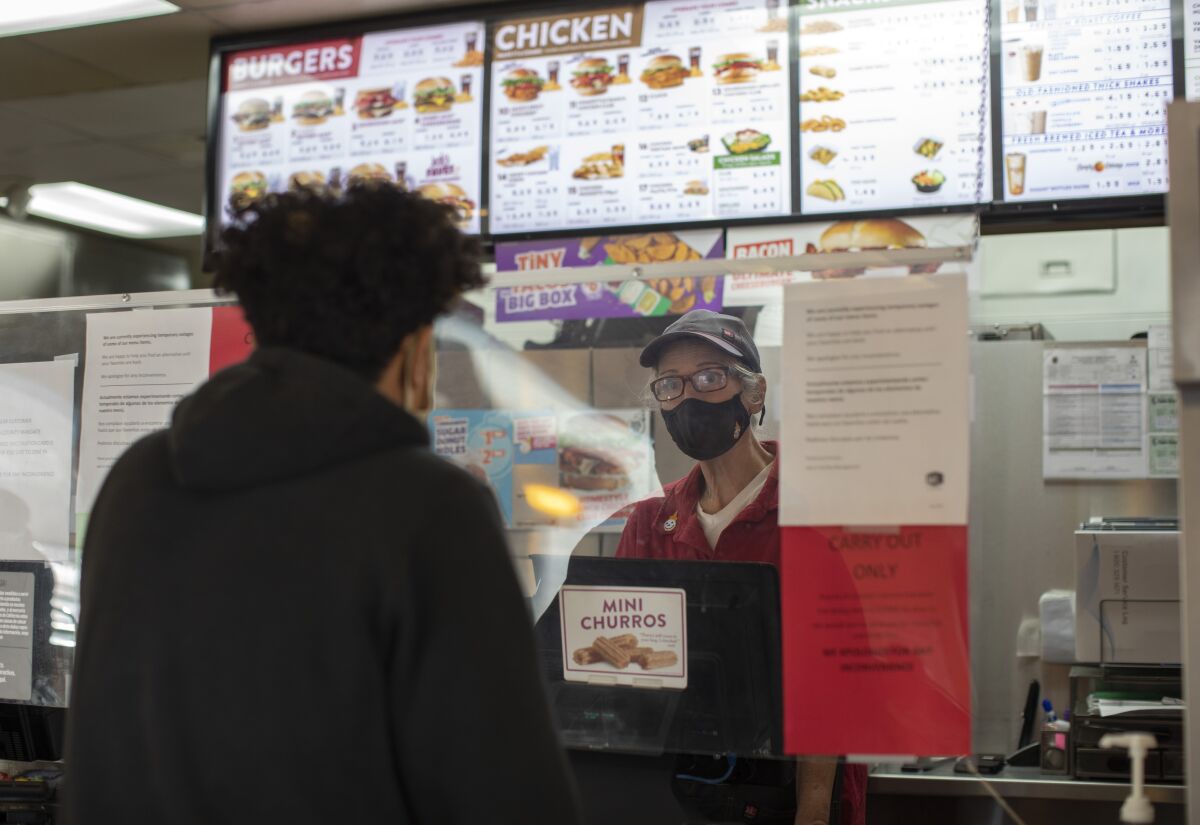 A person in a mask stands at a counter and takes someone's order.