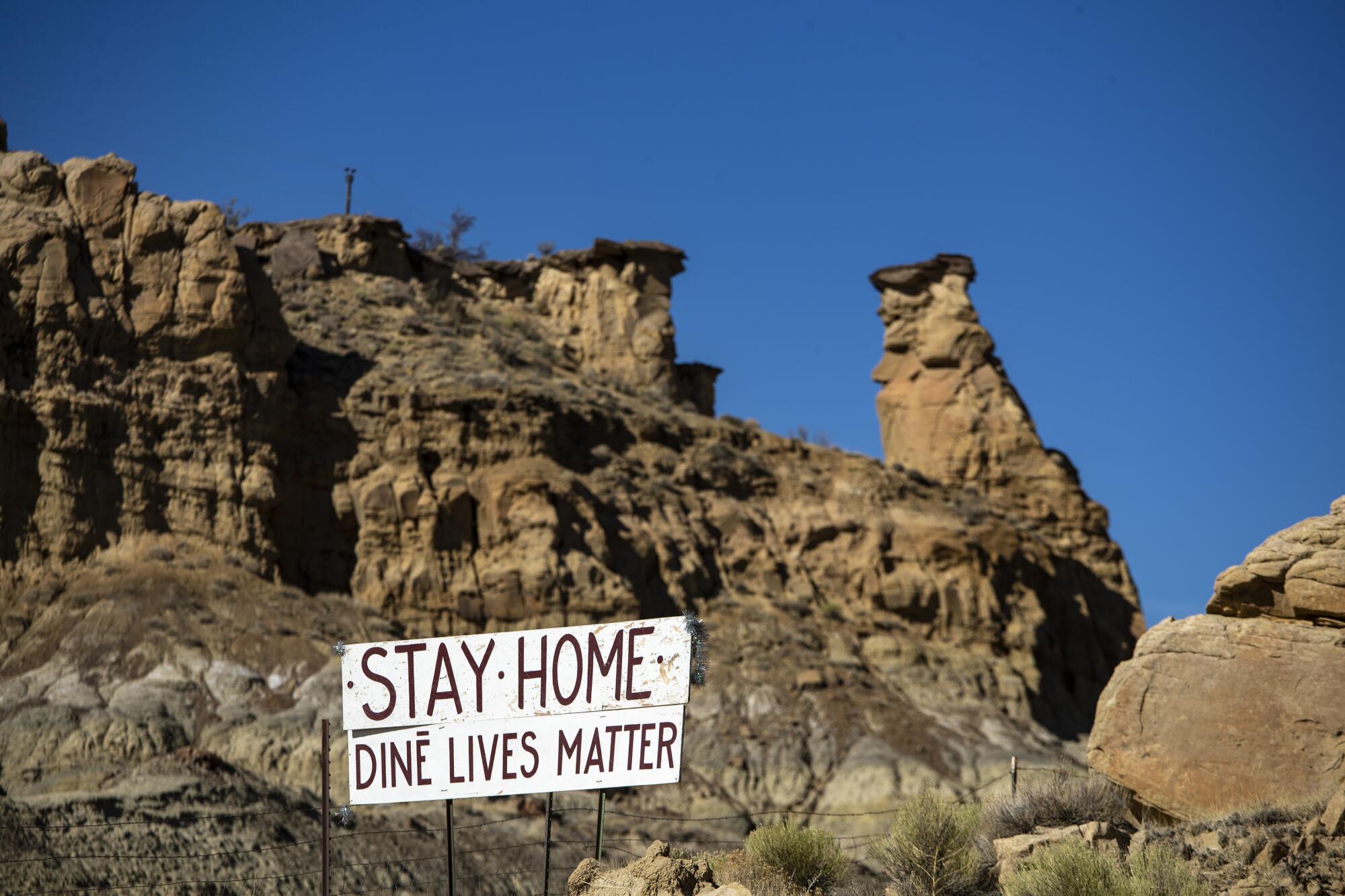 Sign saying "Stay Home, Diné Lives Matter" posted in front of a rock formation.