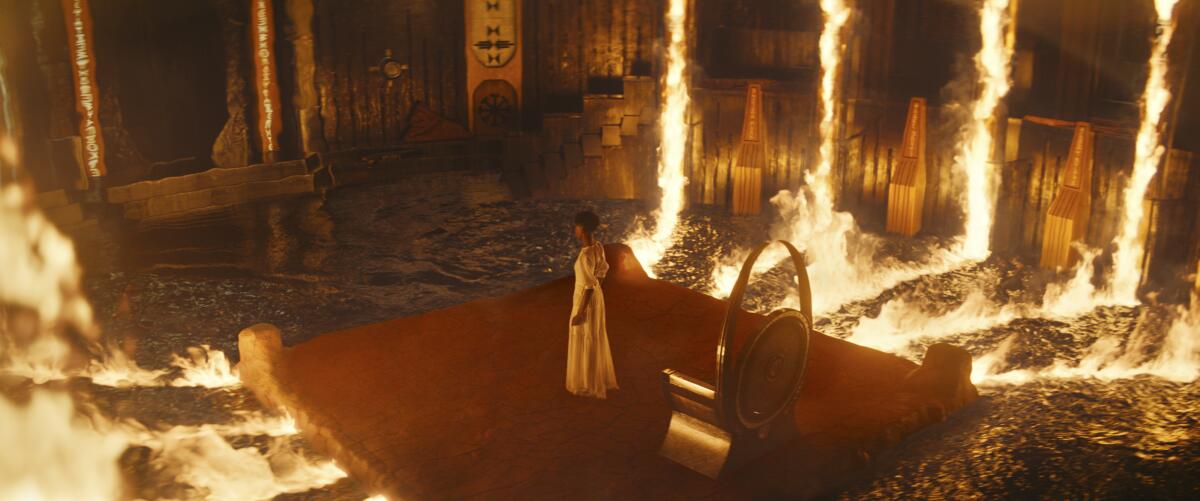 W woman in a white dress stands on platform surrounded in fire