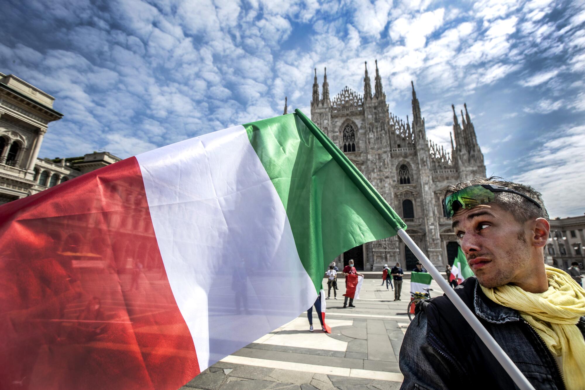 A man holds an Italian flag in front of the Duomo cathedral in Milan on Monday. Italy has begun allowing citizens to return to work and easing restrictions imposed to stem COVID-19 infections.