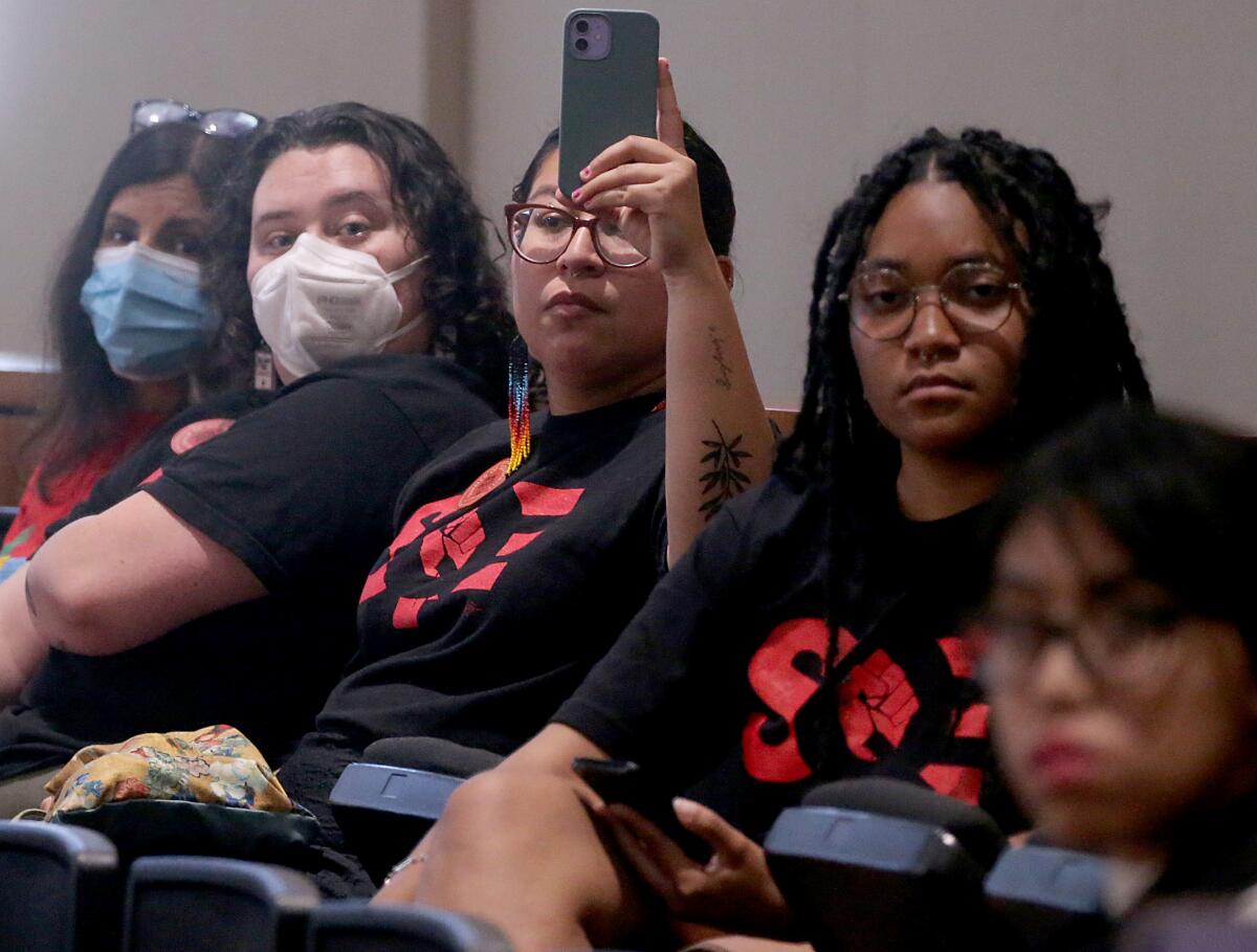 Several students wearing shirts with the letters "SQE" on them, some with masks on, sit in a row of seats.