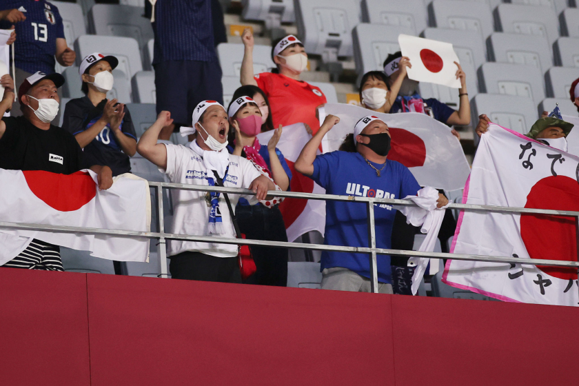 A fan lowers their mask to cheer as others hold up Japanese flags during a soccer event at the Tokyo Olympics.