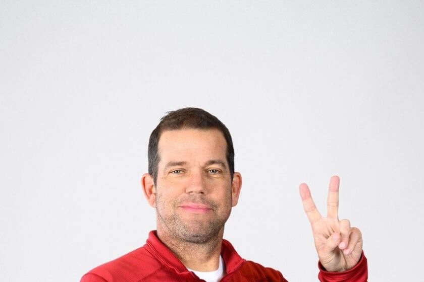 USC coach Dave Nichol holds a football in one hand while holding up two fingers in "V" shape.  