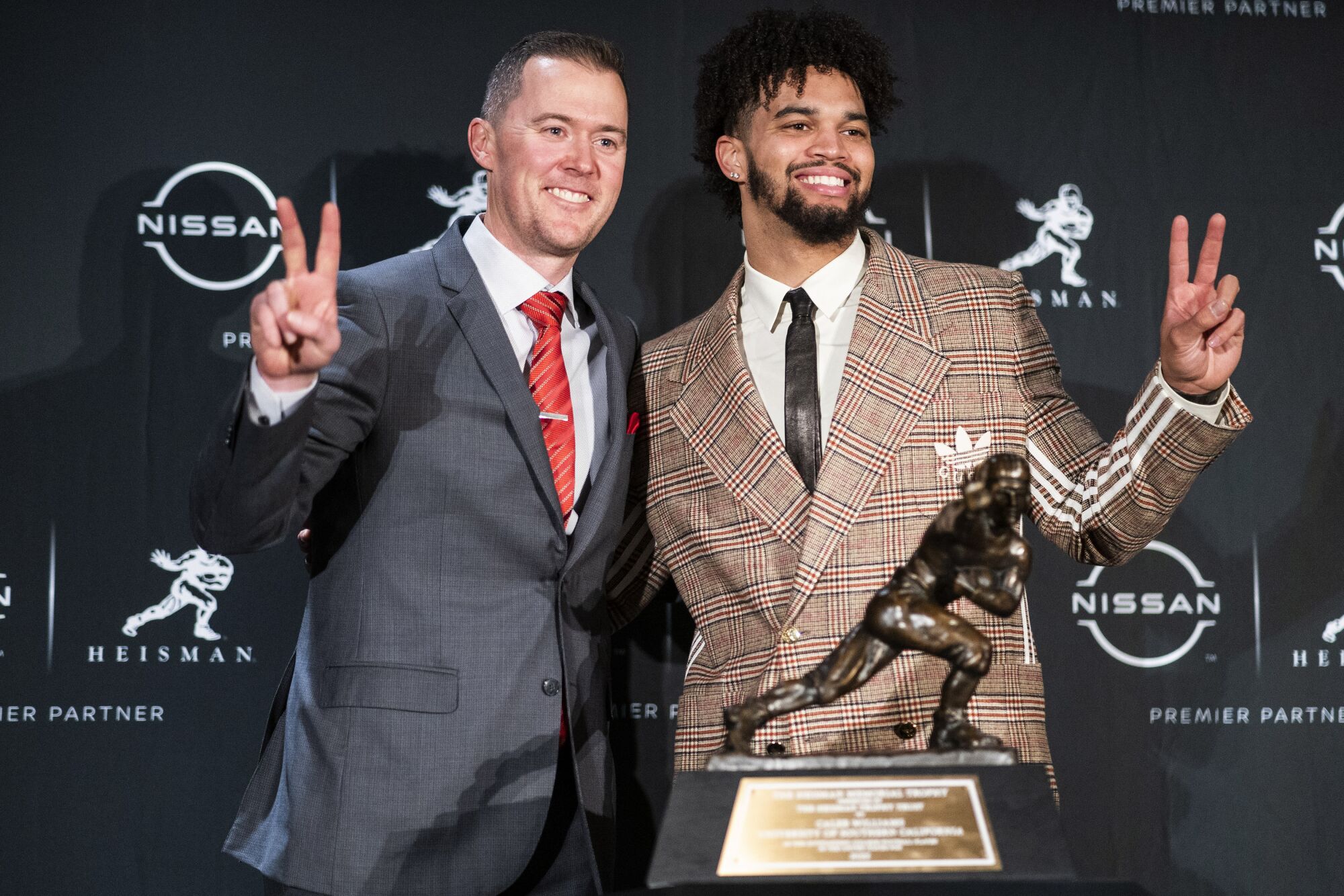 USC quarterback Caleb Williams, right, and Trojans coach Lincoln Riley smile and pose with the Heisman Trophy.