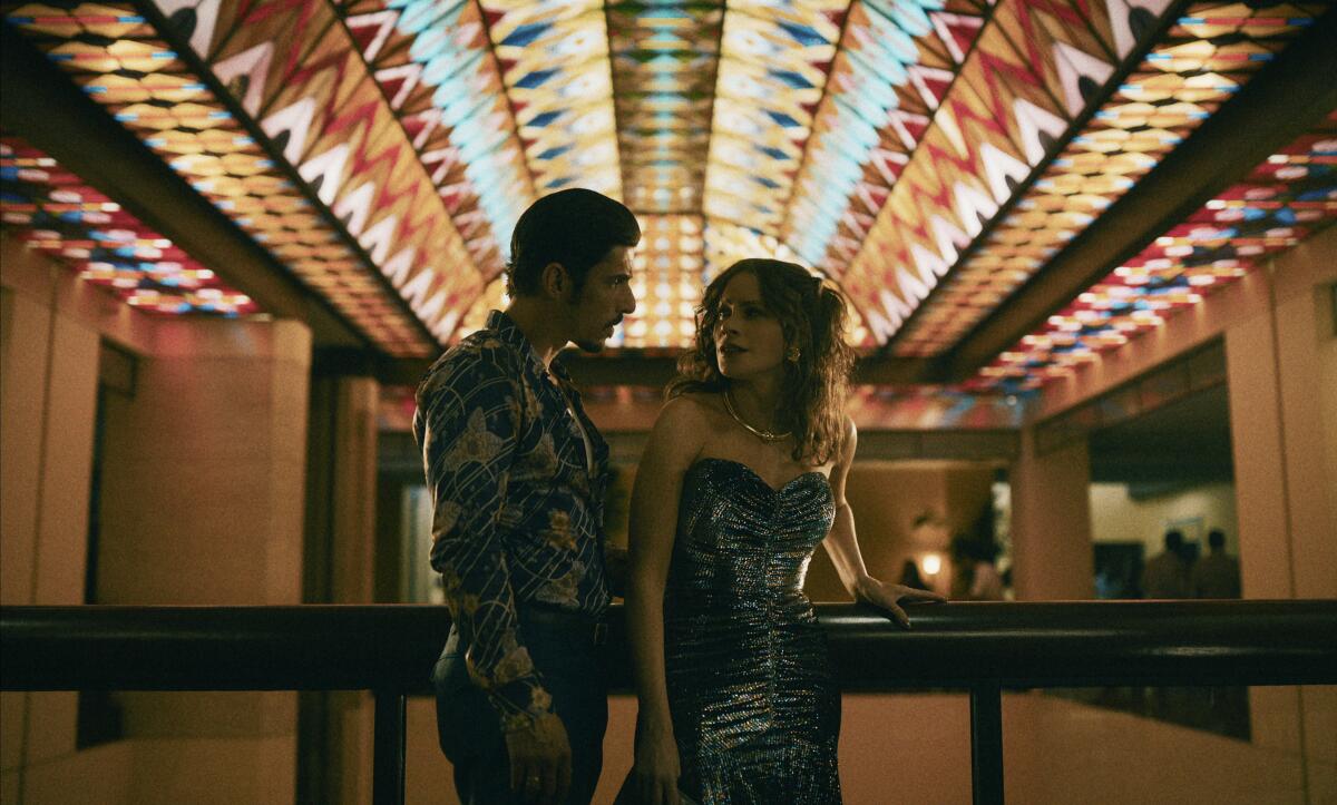 A man in a shiny shirt and a woman in a sparkling dress are framed by an illuminated ceiling redolent of the disco era.