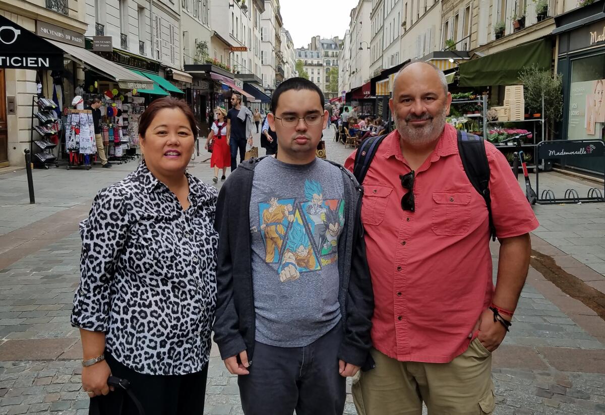 Former Times sports reporter Chris Foster, right, stands beside his wife, Gay, and son, Mark, in Paris in 2021.