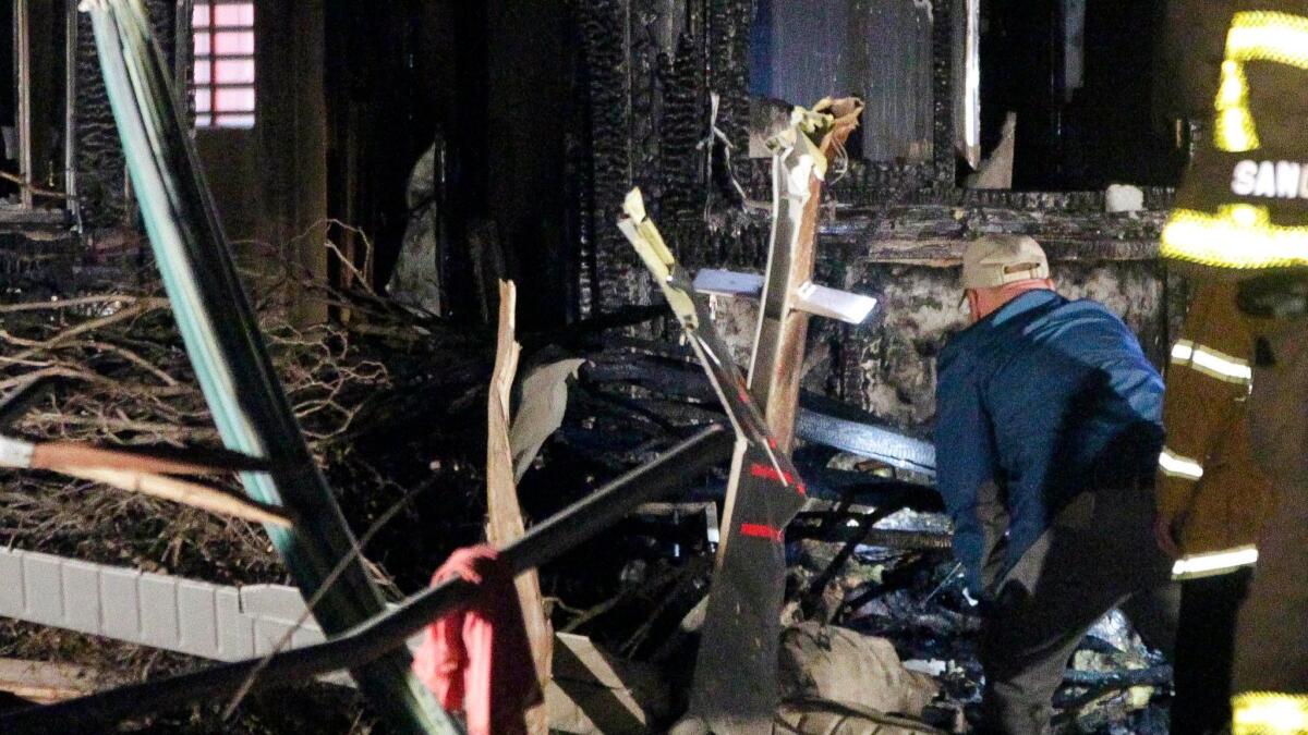 An investigator standing next to the tail section looks at the charred remains of a small plane that crashed into a house in San Diego.