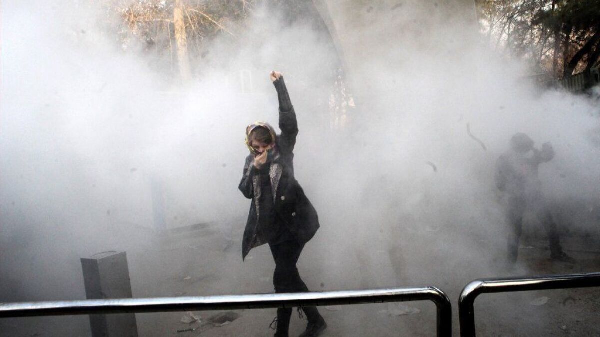 An Iranian woman raises her fist amid the smoke of tear gas during an antigovernment protest at the University of Tehran.