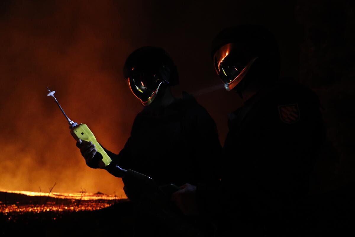 In this photo made available by Ume (Unidad Militar de Emergencias), Military Emergency Unit personal take gas reading measurements near a volcano on the Canary island of La Palma, Spain, in the early hours of Tuesday Sept. 28, 2021. Lava flowing from an erupting volcano on the Spanish island of La Palma has picked up pace on its way to the sea. Officials say it is now within about 800 meters (875 yards) of the shoreline. When the molten rock eventually meets the sea water it could trigger explosions and toxic gas. (Luismi Ortiz/UME via AP)