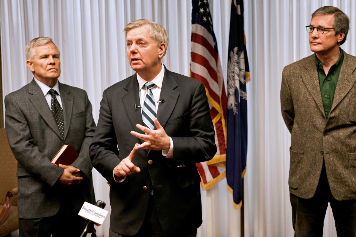 The Rev. Jim Goodroe, left, listens while Sen. Lindsey Graham speaks about immigration reform in Columbia, S.C., in March. At right is Hal Stevenson, owner of Grace Outdoor.