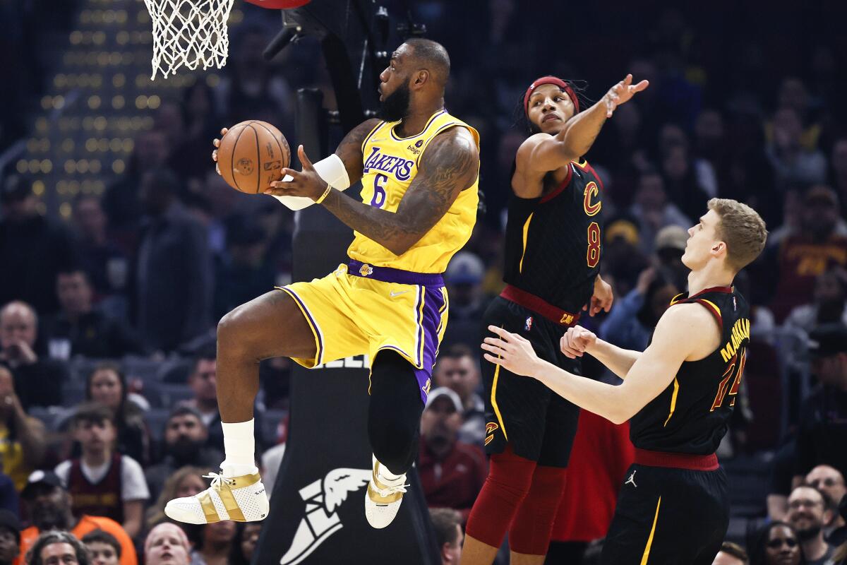 Lakers forward LeBron James soars past Cavaliers forwards Lamar Stevens (8) and Lauri Markkanen (24) for a layup.