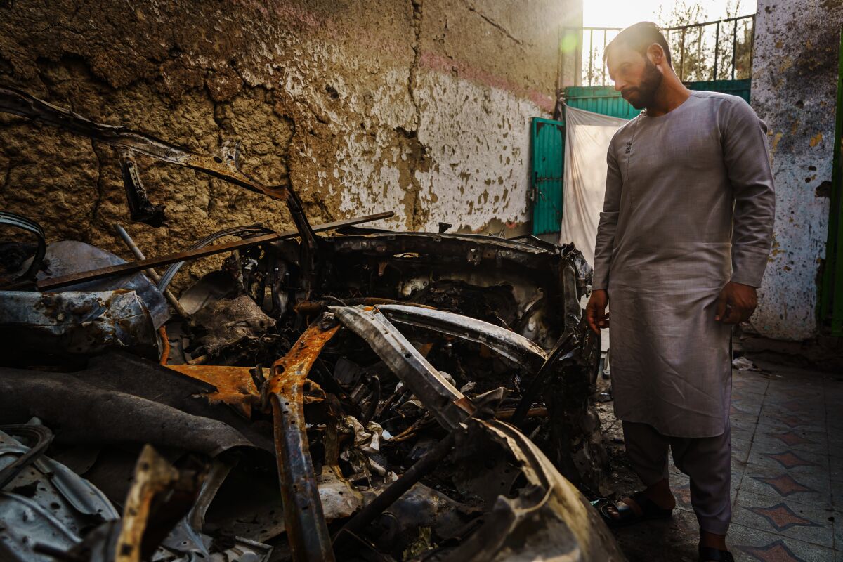A man surveys remains of a car destroyed in a drone strike 