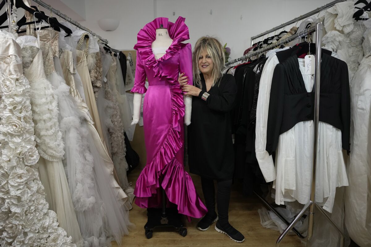 La diseñadora británica Elizabeth Emanuel abraza una réplica de un vestido de noche que diseñó para la entonces 