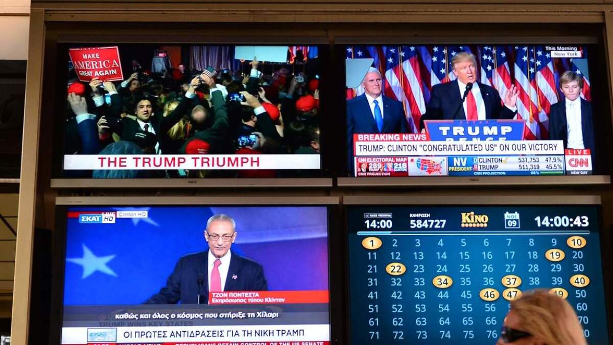 A woman walks past TV monitors displaying results of the U.S. presidential elections at an outdoor cafe in Athens on Nov. 9.