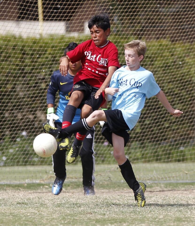 Newport Heights' Cameron Harper, right, tries to boot it into the goal as Wilson's Miguel Pena, left, disrupts the play, during the boys' 5-6 gold division championship game at the Daily Pilot Cup Sunday.